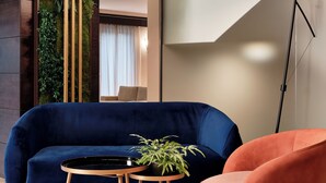 A modern living room with a dark blue sofa, a round wooden table with a plant, and a pink armchair. - Crowne Plaza Milan - Malpensa Airport by IHG (Somma Lombardo)