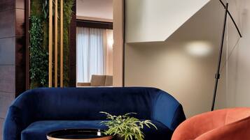 Un salon moderne avec un canapé bleu foncé, une table ronde en bois ornée d’une plante et un fauteuil rose.