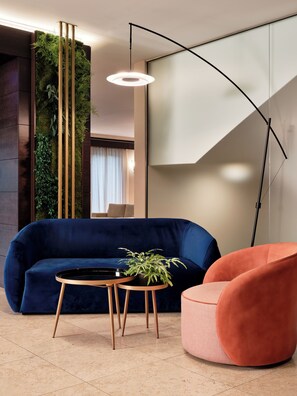 Un salón moderno con un sofá azul oscuro, una mesa redonda de madera con una planta y un sillón rosa.