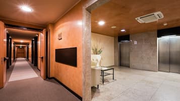 Un pasillo de hotel con una recepción, un tablón informativo en la pared y un ascensor.