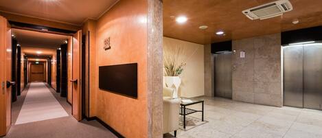 Un pasillo de hotel con una recepción, un tablón informativo en la pared y un ascensor.