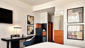 Una habitació d'hotel moderna amb un llit gran, una taula de treball amb una cadira, televisió de pantalla plana i obres d'art a les parets.
