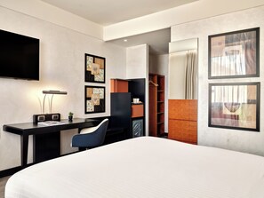 A modern hotel room with a large bed, a desk with a chair, a flat-screen TV, and artwork on the walls.