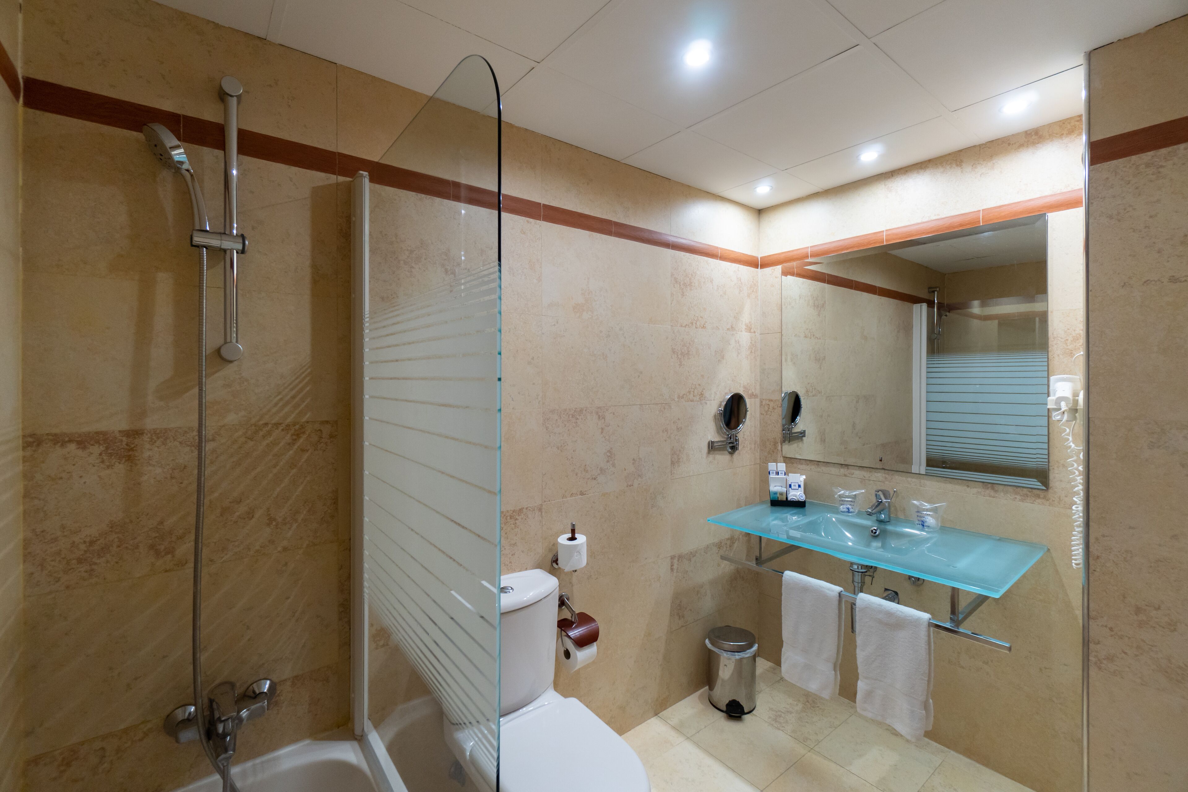 Un baño moderno con ducha envuelta en vidrio, inodoro blanco, lavabo de vidrio y espejo sobre el lavabo.