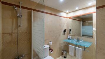 Un baño moderno con ducha envuelta en vidrio, inodoro blanco, lavabo de vidrio y espejo sobre el lavabo.
