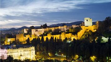 A historic walled city with a prominent castle on a hill, surrounded by trees and illuminated buildings.