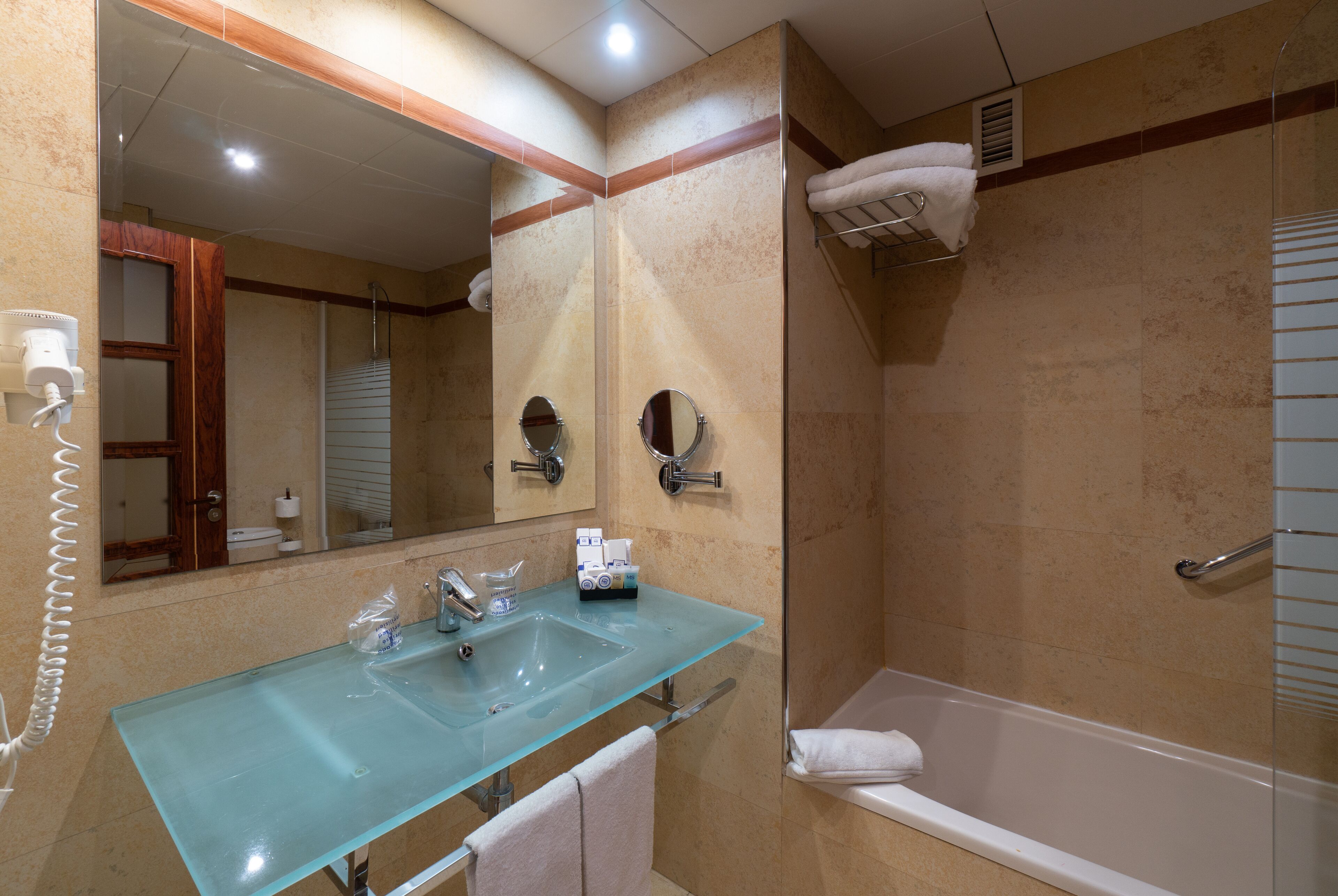 A bathroom with a glass sink, a mirror, a towel rack, and a shower area.