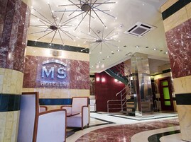 Un vestíbulo de hotel con un mostrador de recepción de mármol, una escalera y un candelabro moderno.
