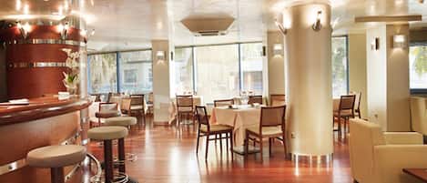 A restaurant interior with wooden flooring, bar stools, tables, and chairs.