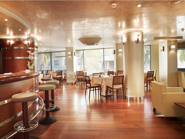 Interior de restaurante con suelo de madera, taburetes de bar, mesas y sillas.