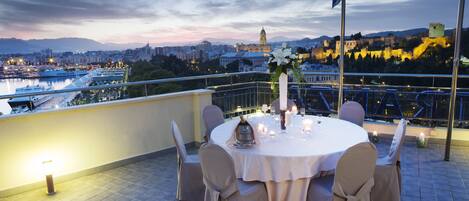 A rooftop terrace with a round table set for dining, overlooking a cityscape with historic buildings and a river.