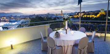 Terraza en la azotea con una mesa redonda dispuesta para comer, con vistas a un paisaje urbano con edificios históricos y un río.
