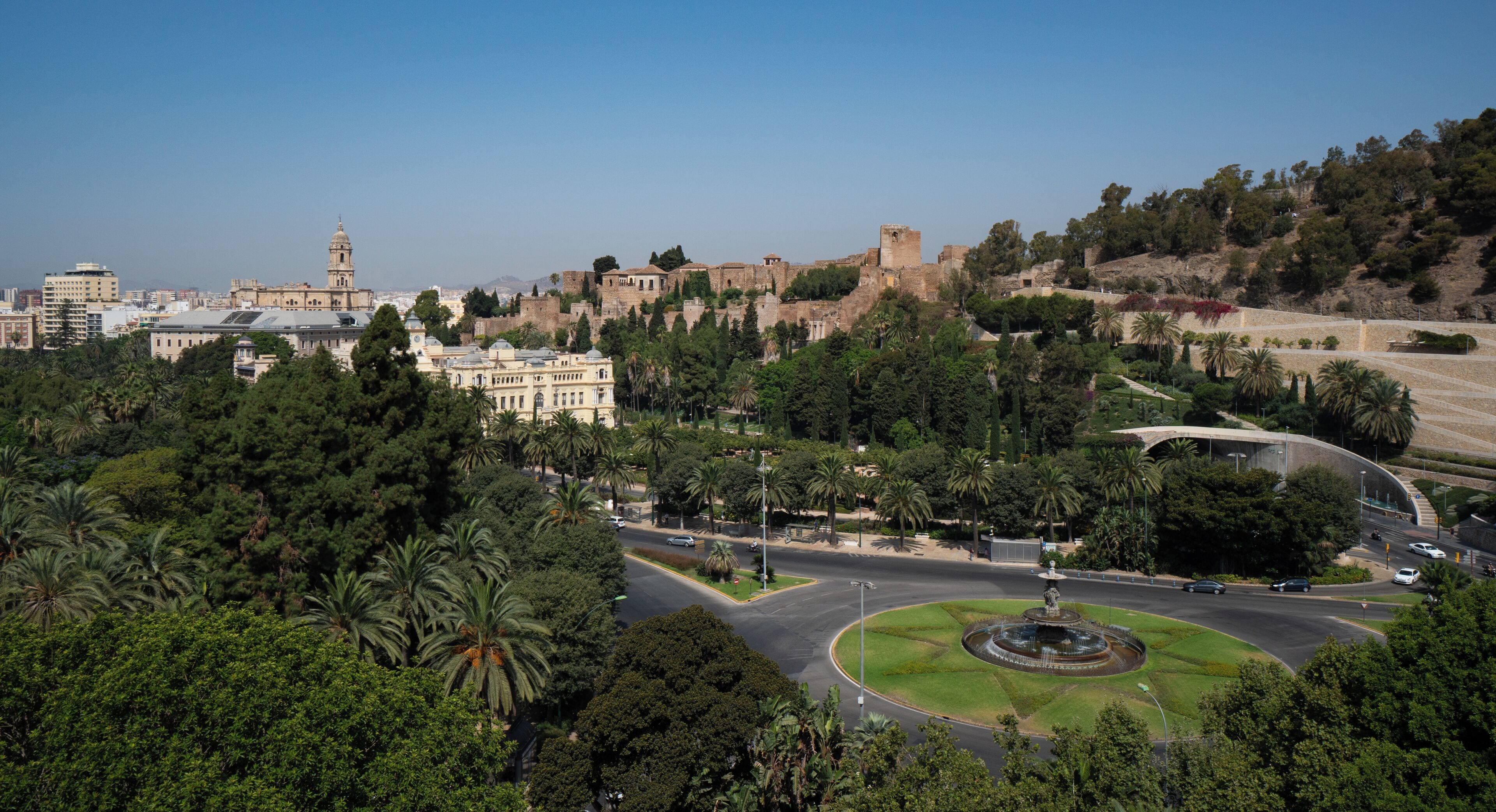 A cityscape with a prominent historical building, a roundabout with a fountain, and lush greenery.