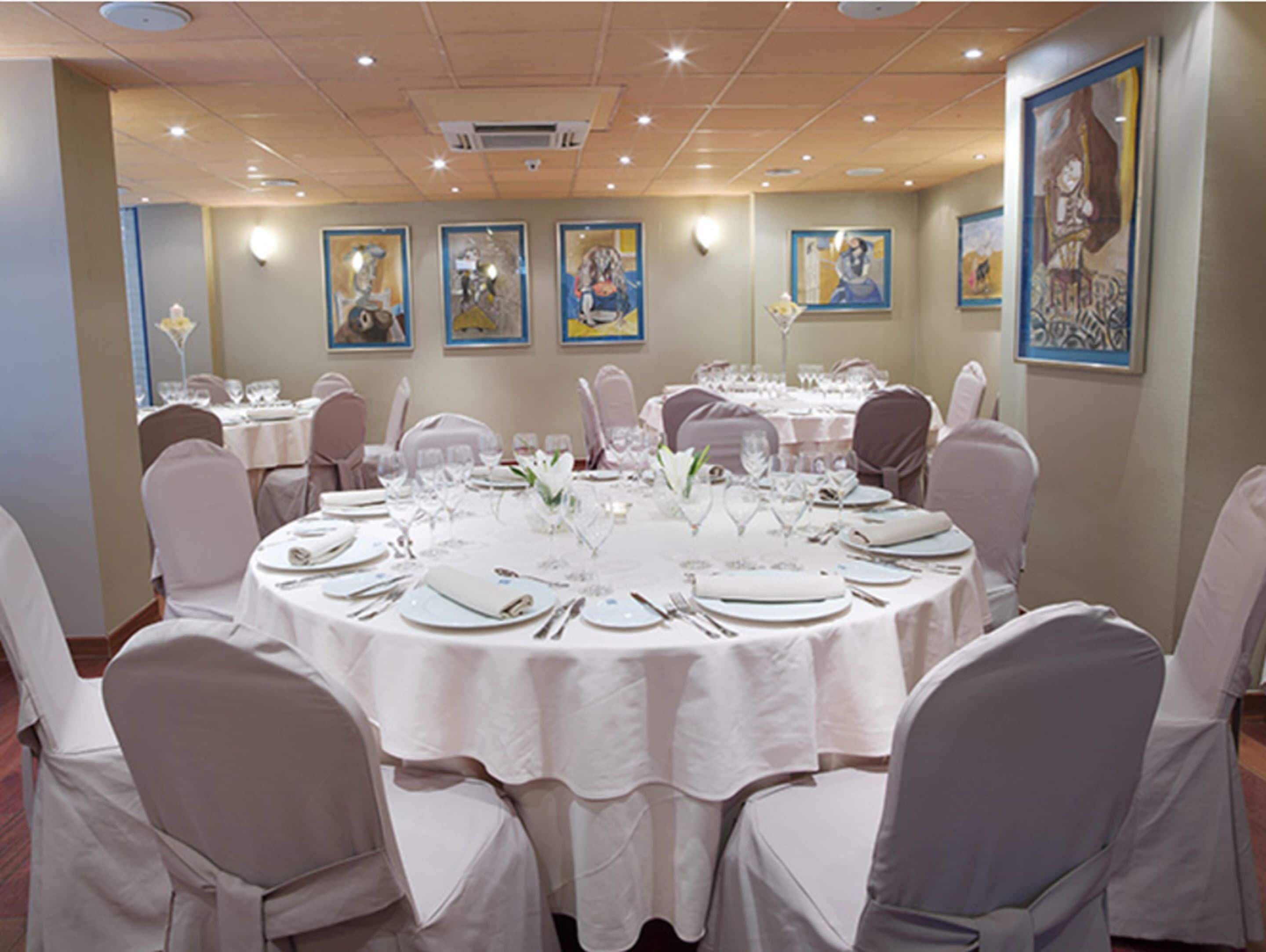 A banquet hall with round tables set for dining, white tablecloths, and chairs with white covers.