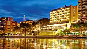 A waterfront hotel with multiple floors, balconies, and a reflection in the water. - Flamboyan Caribe Hotel & Spa (Calvia)