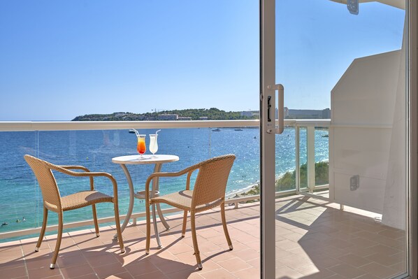 A balcony with wicker chairs and a small table, overlooking a clear blue sea and a distant shoreline. - Flamboyan Caribe Hotel & Spa (Calvia)