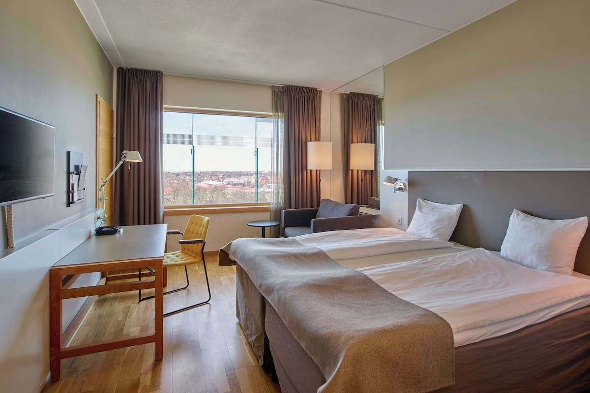 Quarto de hotel com uma cama grande, uma mesa, uma cadeira, uma TV e vista para a cidade.