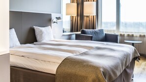 A modern hotel room with a large bed, a seating area with a table, and a view through the window. - Scandic Talk Hotel (Älvsjö)