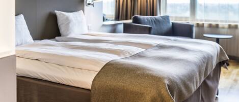 Una habitación de hotel moderna con una cama grande, una zona de estar con una mesa y vistas al exterior.