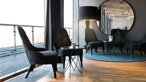 A modern lounge area with a round table, two chairs, a lamp, and a large mirror on the wall. - Scandic Talk Hotel (Älvsjö)
