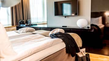 A hotel room with a bed, a desk with a flat-screen TV, a lamp, and a window with curtains.