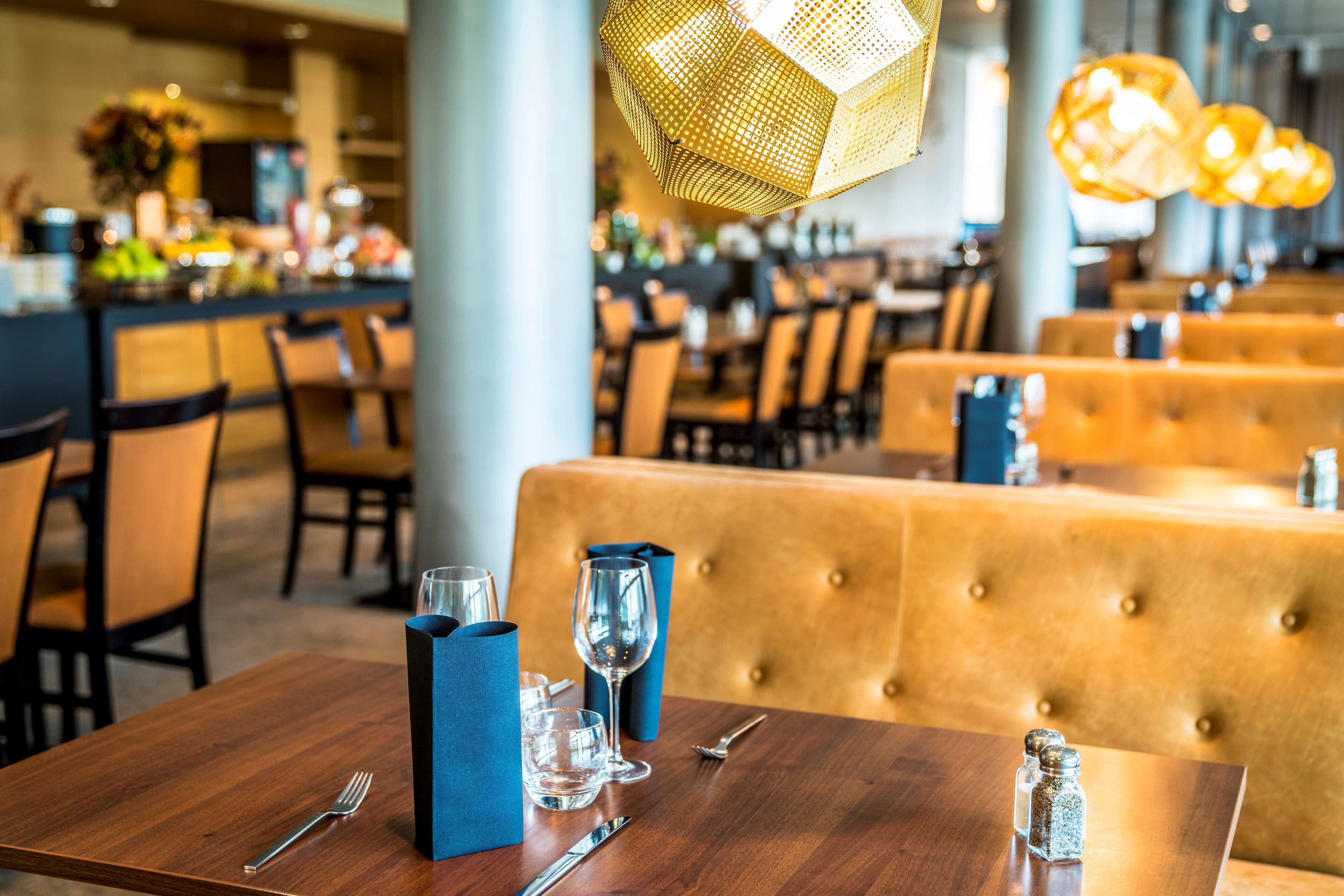 Un interior de restaurante con mesas de madera, servilletas azules e iluminación colgante dorada.