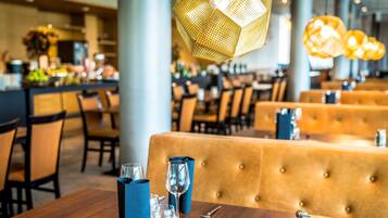 Un interior de restaurante con mesas de madera, servilletas azules e iluminación colgante dorada.