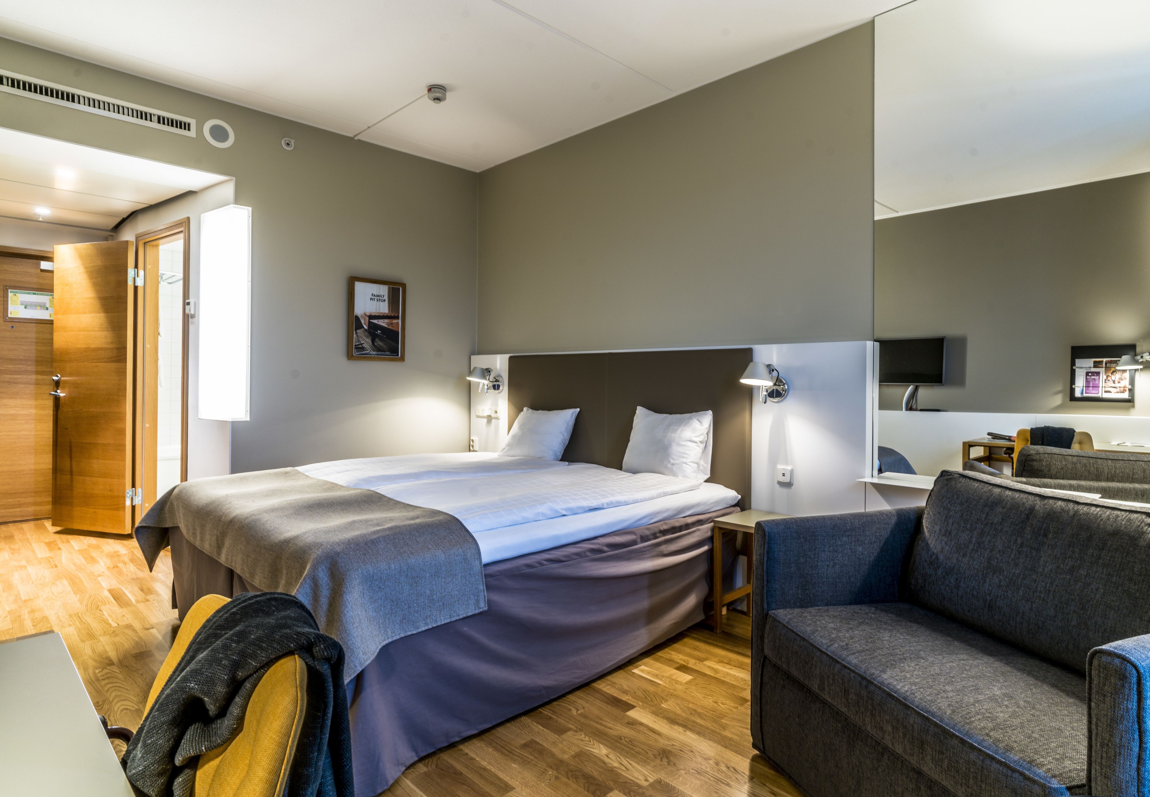 A modern hotel room with a large bed, a sofa, a desk, and a television.