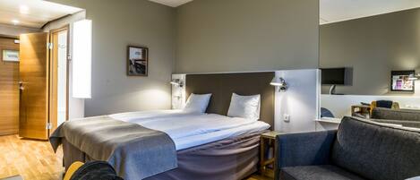 A modern hotel room with a large bed, a sofa, a desk, and a television.