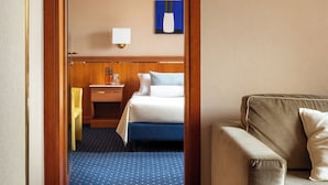 Ein Hotelzimmer mit einem Bett, einem Schreibtisch, einem Sessel, einer Couch, einer Lampe und einem gerahmten Bild an der Wand.