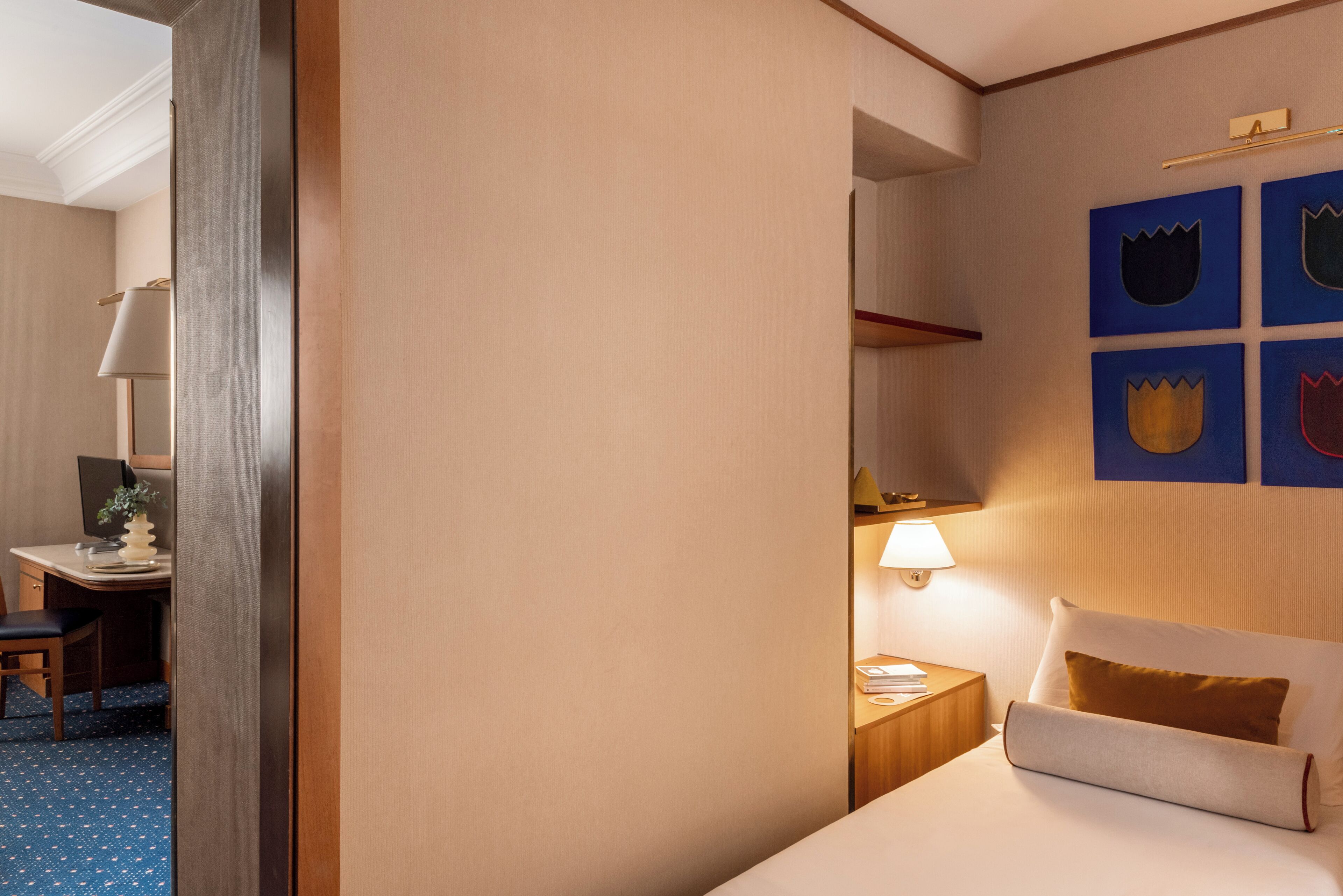 Una camera d'albergo con un letto, un comodino, una lampada e una scrivania con una sedia.