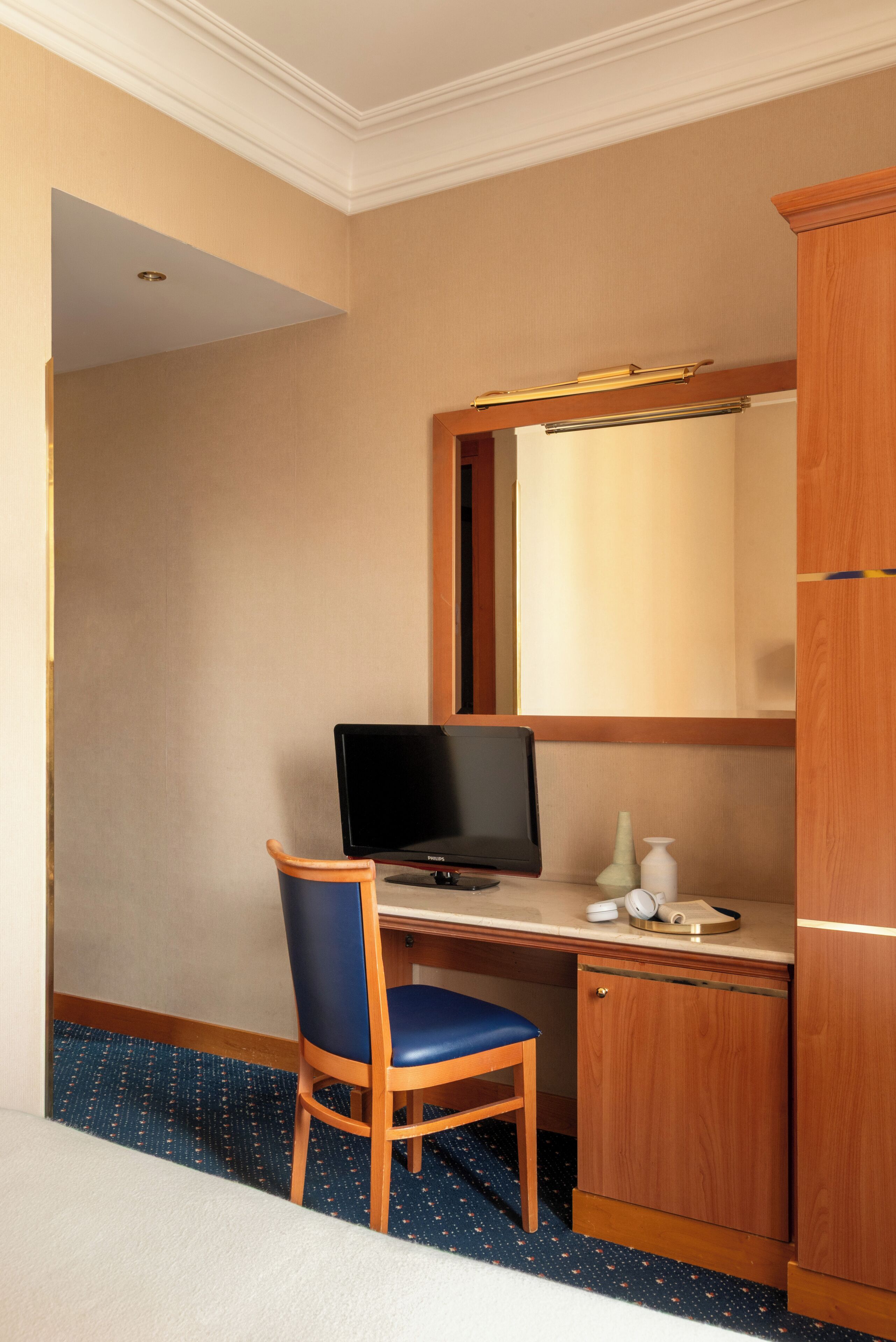 Camera d'albergo con una scrivania in legno, un computer, una sedia, un mobiletto e uno specchio.