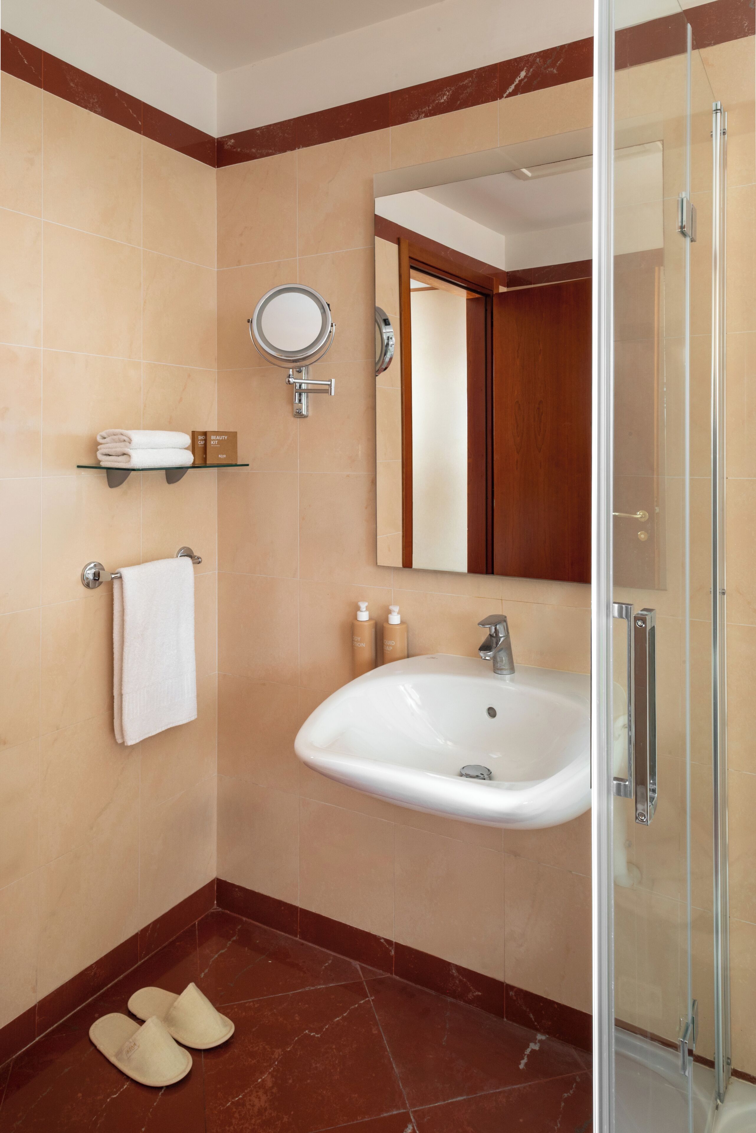 Un baño moderno con cabina de ducha de vidrio, un lavabo blanco, un espejo redondo y un perchero para toallas.