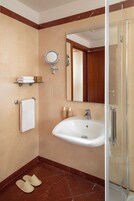A modern bathroom with a glass shower enclosure, a white sink, a round mirror, and a towel rack.
