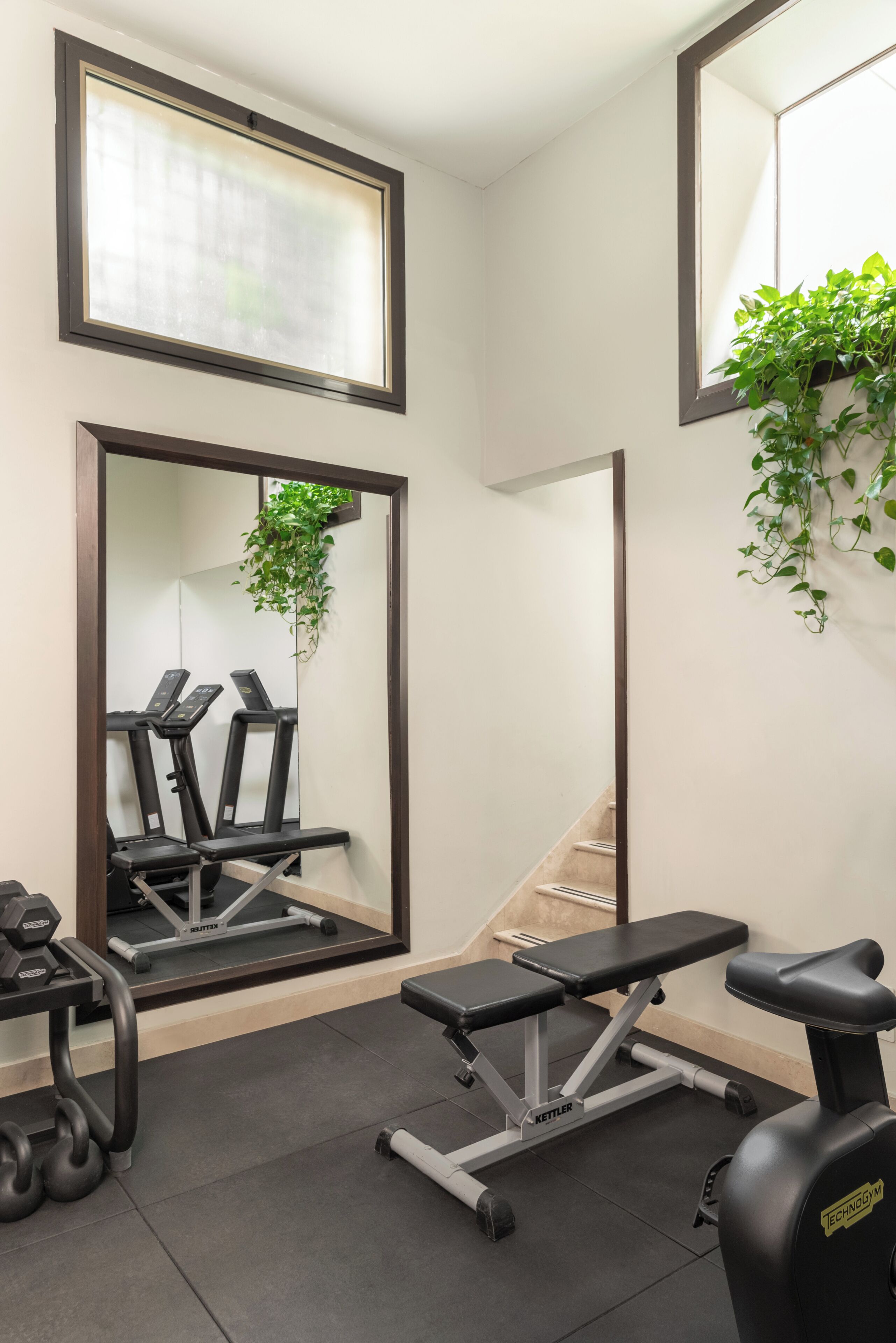 A gym with exercise equipment, mirrors, and a staircase.