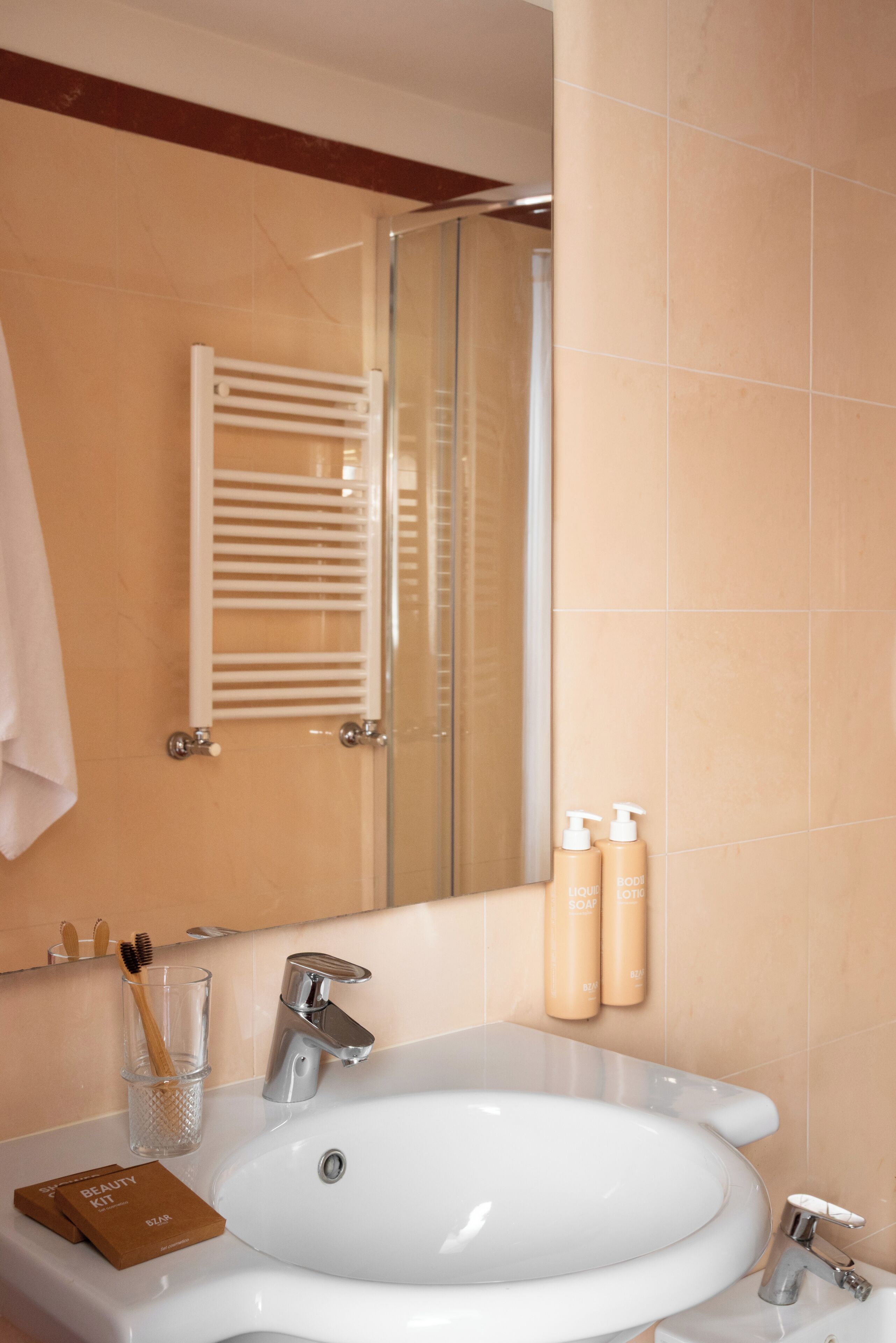 Un bagno con un lavandino bianco, uno specchio, un portasciugamani e due flaconi di sapone.