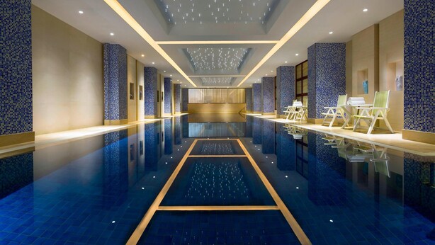 A spacious indoor swimming pool with a central water feature, surrounded by seating areas and decorative lighting. - Courtyard by Marriott Shanghai Fengxian (Shanghai)