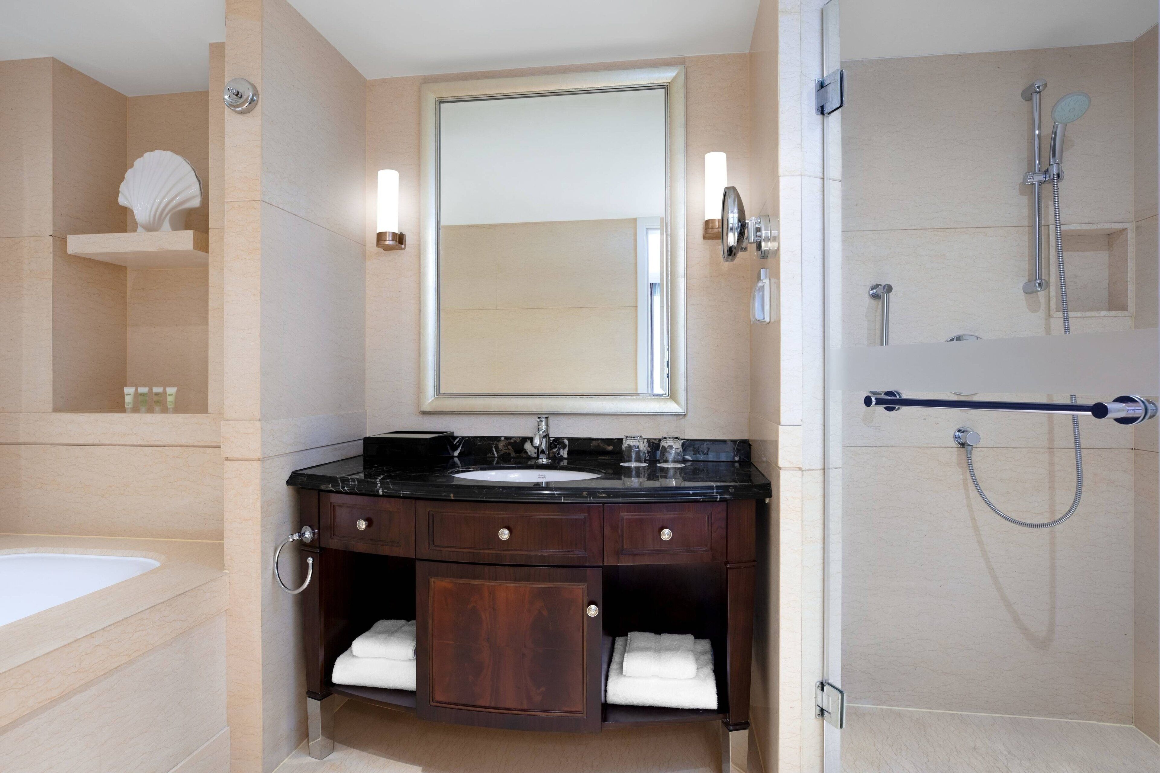 A modern bathroom with a marble sink, a large mirror, and a walk-in shower.