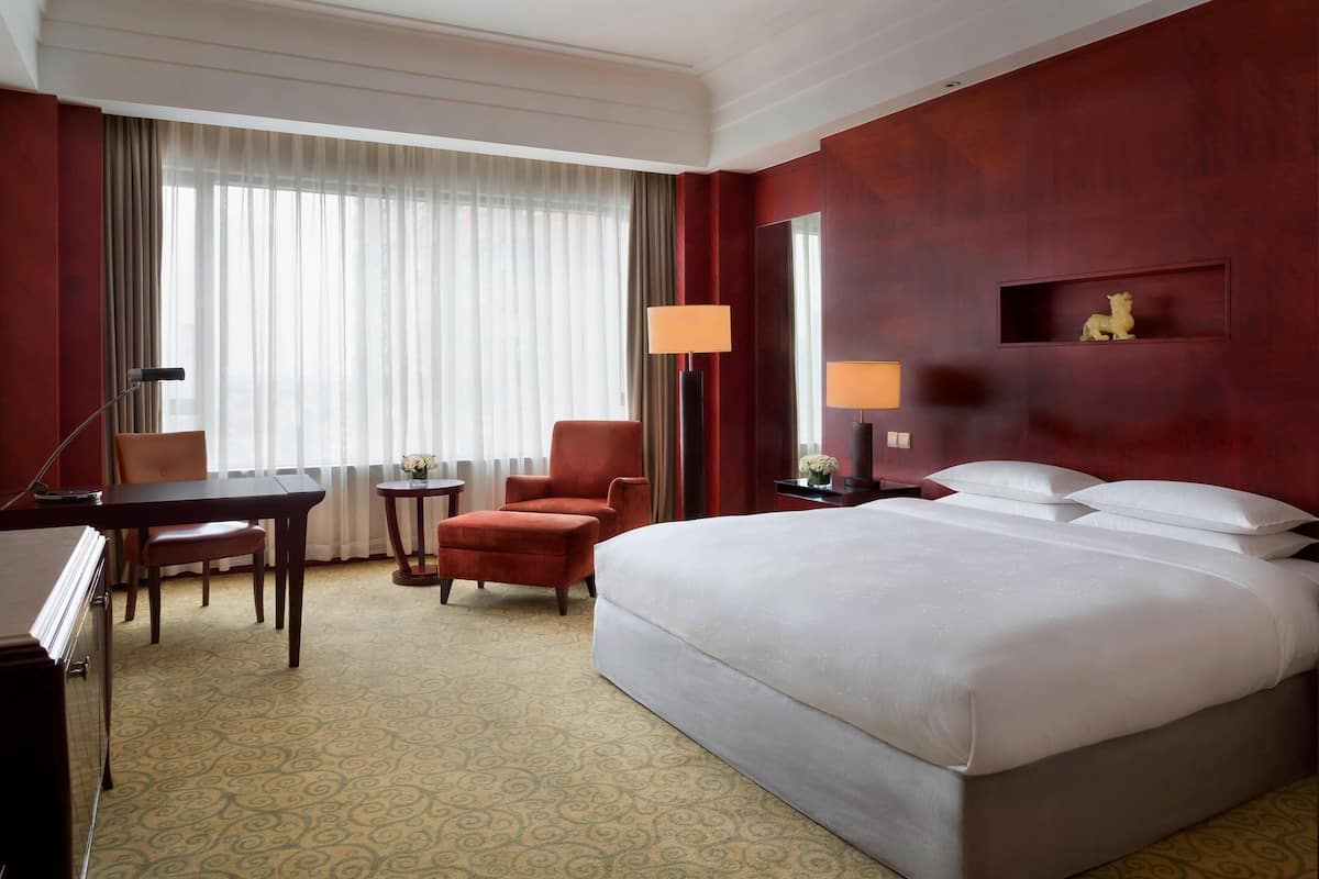 A hotel room with a large bed, a desk, a chair, and a small table.