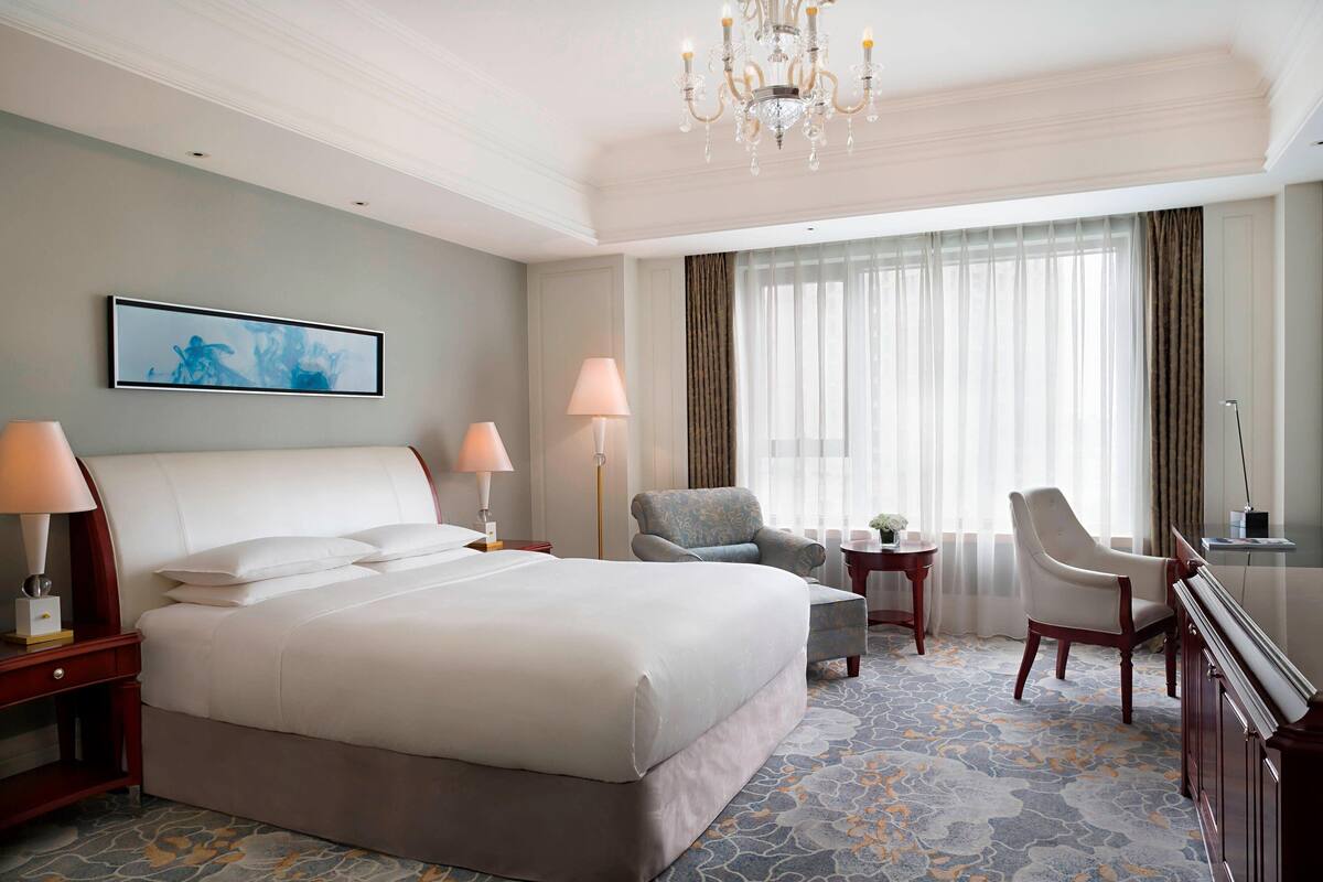 A hotel room with a large bed, two chairs, a desk, and a chandelier.