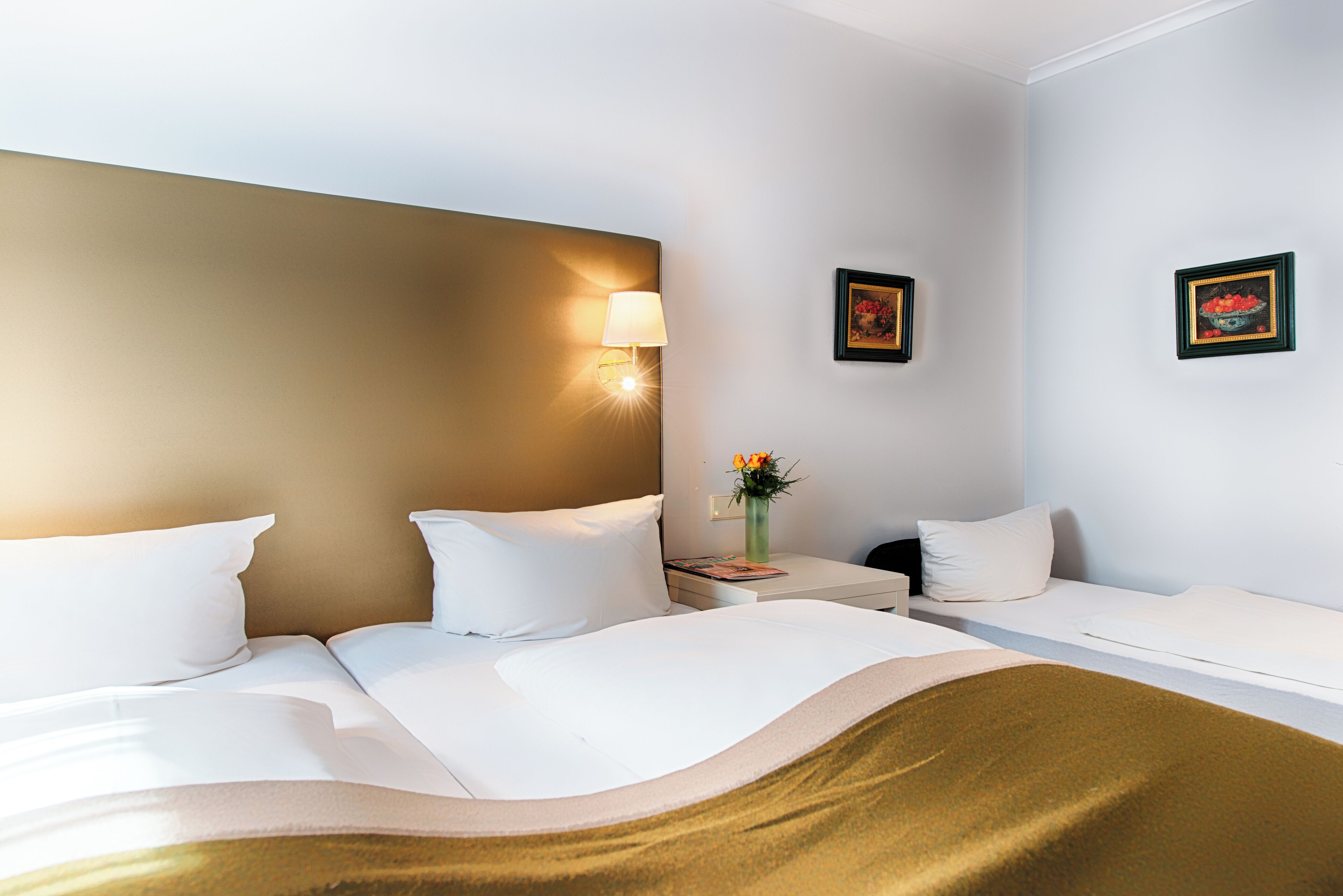 A hotel room with a bed, bedside table, lamp, and two framed pictures on the wall.