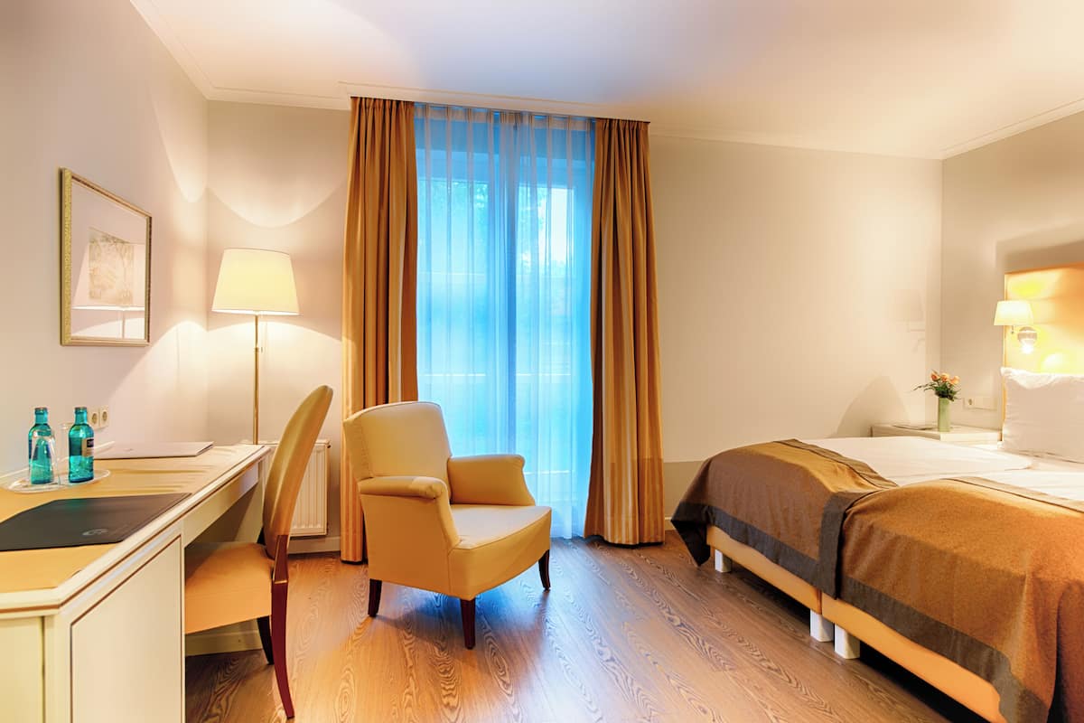 A hotel room with a desk, chair, bed, and a large window with curtains.