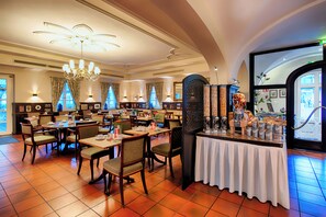 A spacious restaurant with multiple dining tables and chairs, a central bar area, and large windows with curtains. -  Hotel SchreiberHof (Aschheim)
