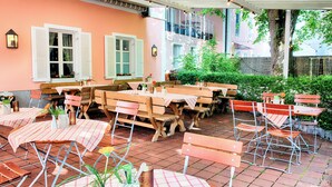 An outdoor patio area with wooden tables and benches, covered by a white canopy.