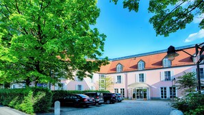 A building with a red roof and pink walls, a cobblestone driveway, and parked cars.