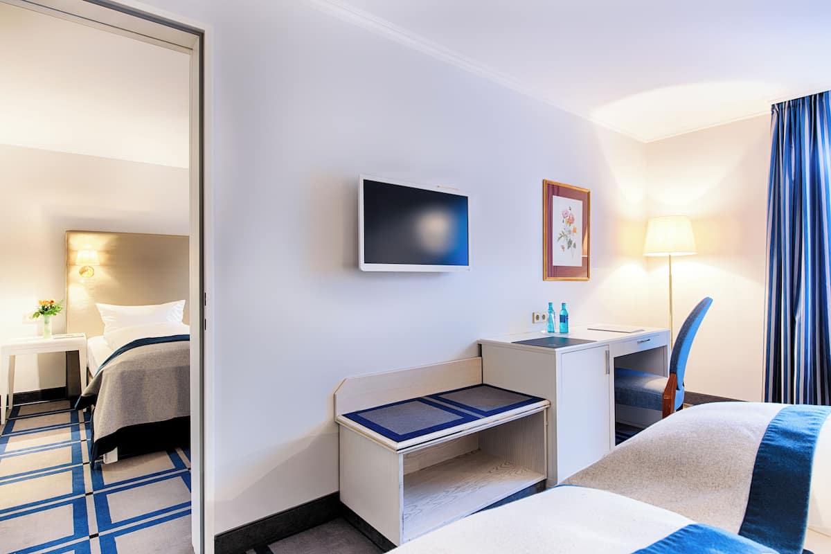 A hotel room with a bed, bedside table, desk, chair, TV, lamp, and a framed picture on the wall.