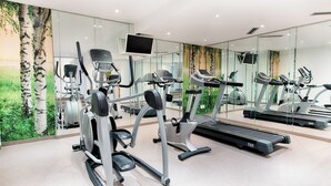 A modern gym with various exercise equipment, including treadmills and elliptical machines, and a large mirror wall.