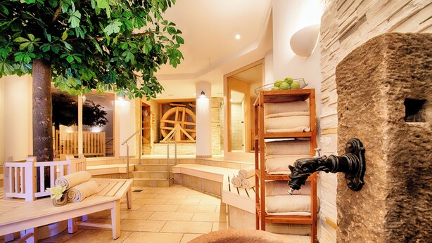A spa area with wooden benches, a stone wall, and a large wooden wheel structure.