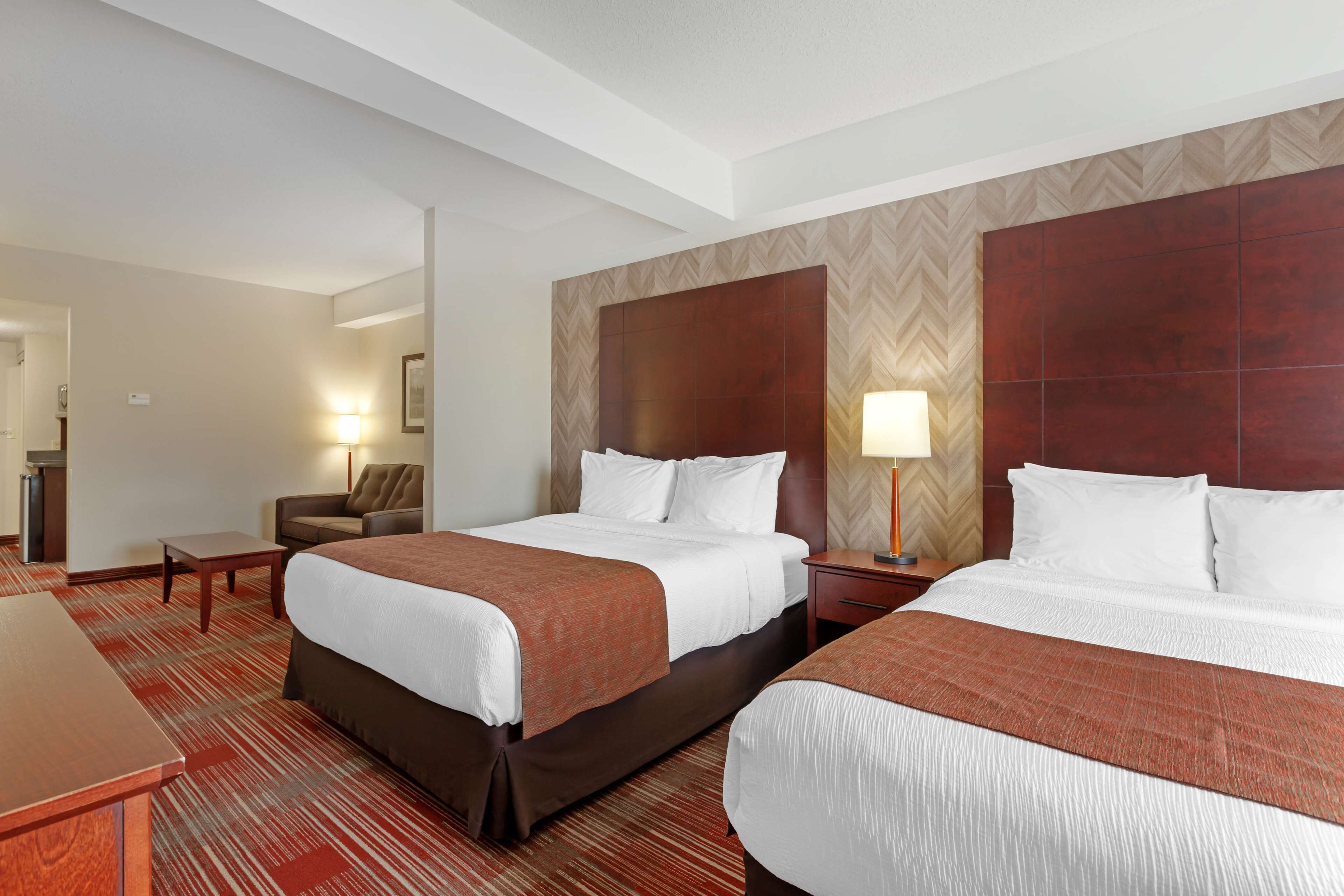 A hotel room with two beds, a desk, a chair, and a nightstand with a lamp.