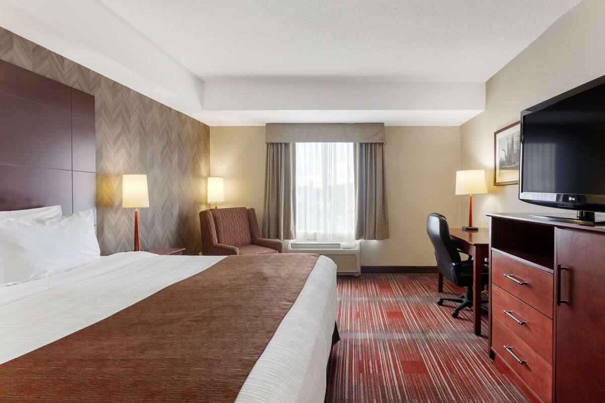 A hotel room with a large bed, a desk with a chair, a television, and two lamps.
